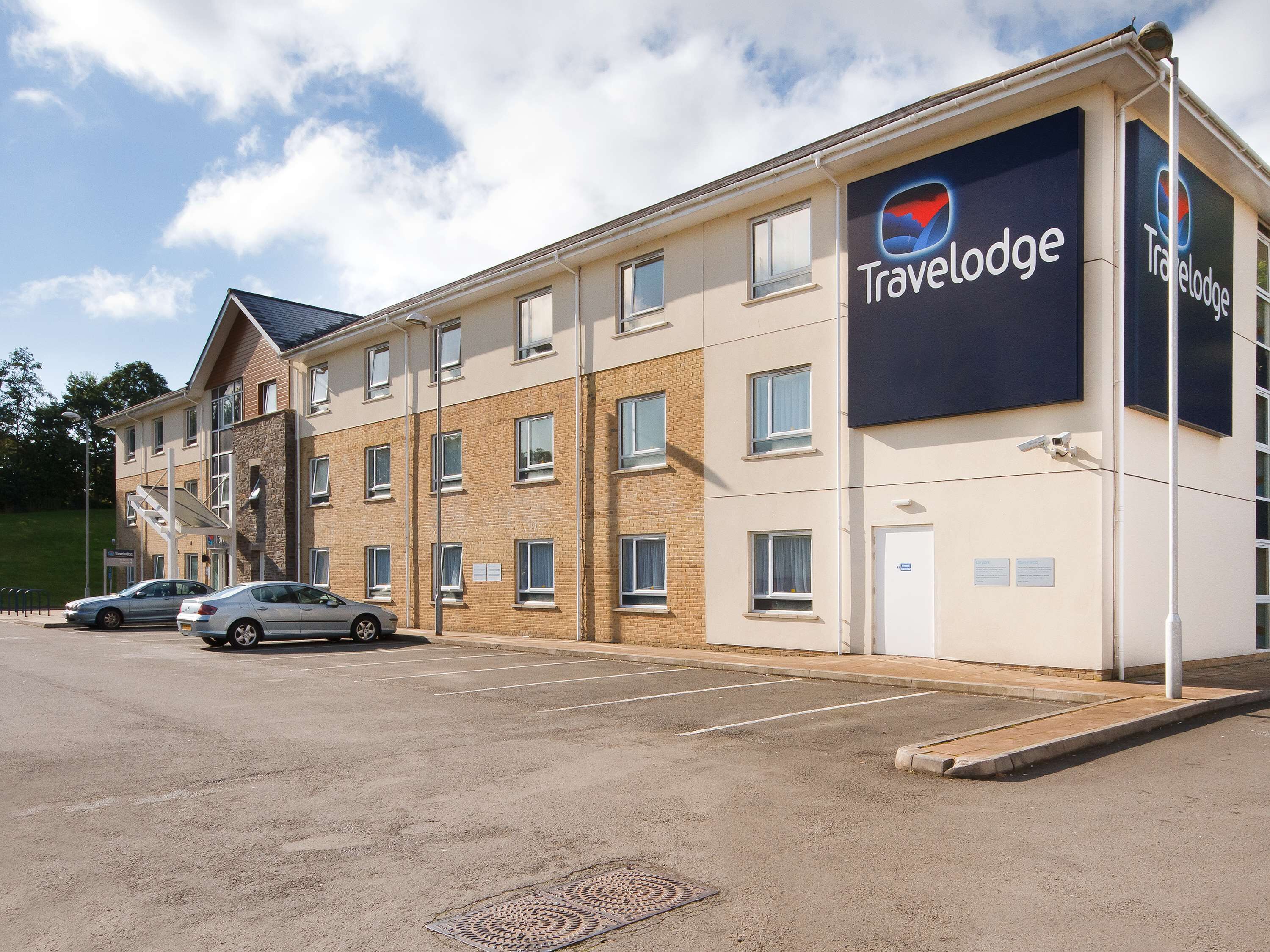 Un hotel Travelodge con fachada de ladrillo, múltiples ventanas y un estacionamiento con dos coches.