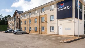 Un hotel Travelodge con fachada de ladrillo, múltiples ventanas y un estacionamiento con dos coches.