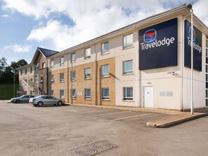Ett Travelodge-hotell med en fasad av tegel, flera fönster och en parkeringsplats med två bilar.