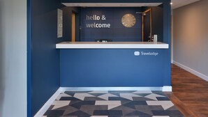Una recepción con un reloj, un cartel que dice 'hola y bienvenidos' y el logotipo de Travelodge.