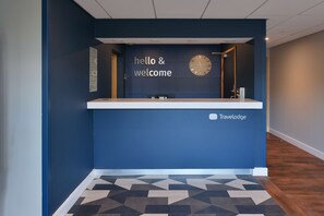 En receptionsdisk med en klocka, en skylt med texten ”välkommen” och Travelodges logotyp.