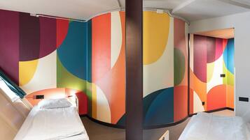 Habitación de hotel con dos camas, una pared curva con motivos abstractos de colores y un ventanal que proporciona luz natural.