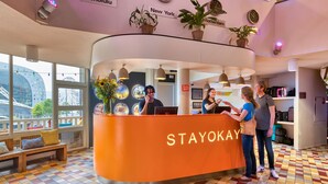 A reception area with a 'STAYOKAY' sign, a check-in counter, and a view of a Ferris wheel through large windows. - Stayokay Rotterdam - Hostel to Stayokay Rotterdam - fully renovated April 2026 (Rotterdam)