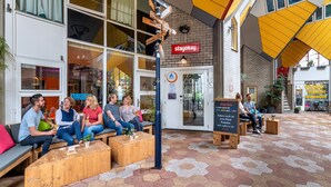 An outdoor seating area with hexagonal patterned flooring, wooden benches, and a signboard with the name "stayokay". - Stayokay Rotterdam - Hostel to Stayokay Rotterdam - fully renovated April 2026 (Rotterdam)