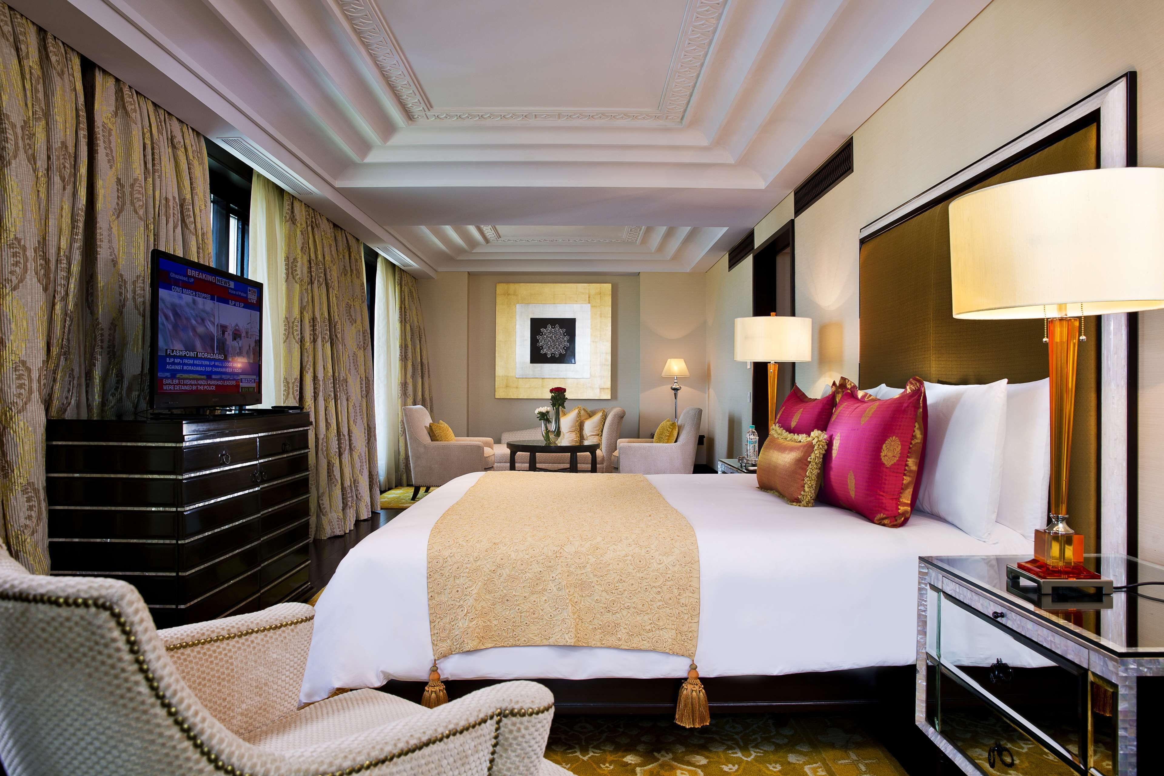 A hotel room with a large bed, a television, a desk with a lamp, and a seating area with chairs.