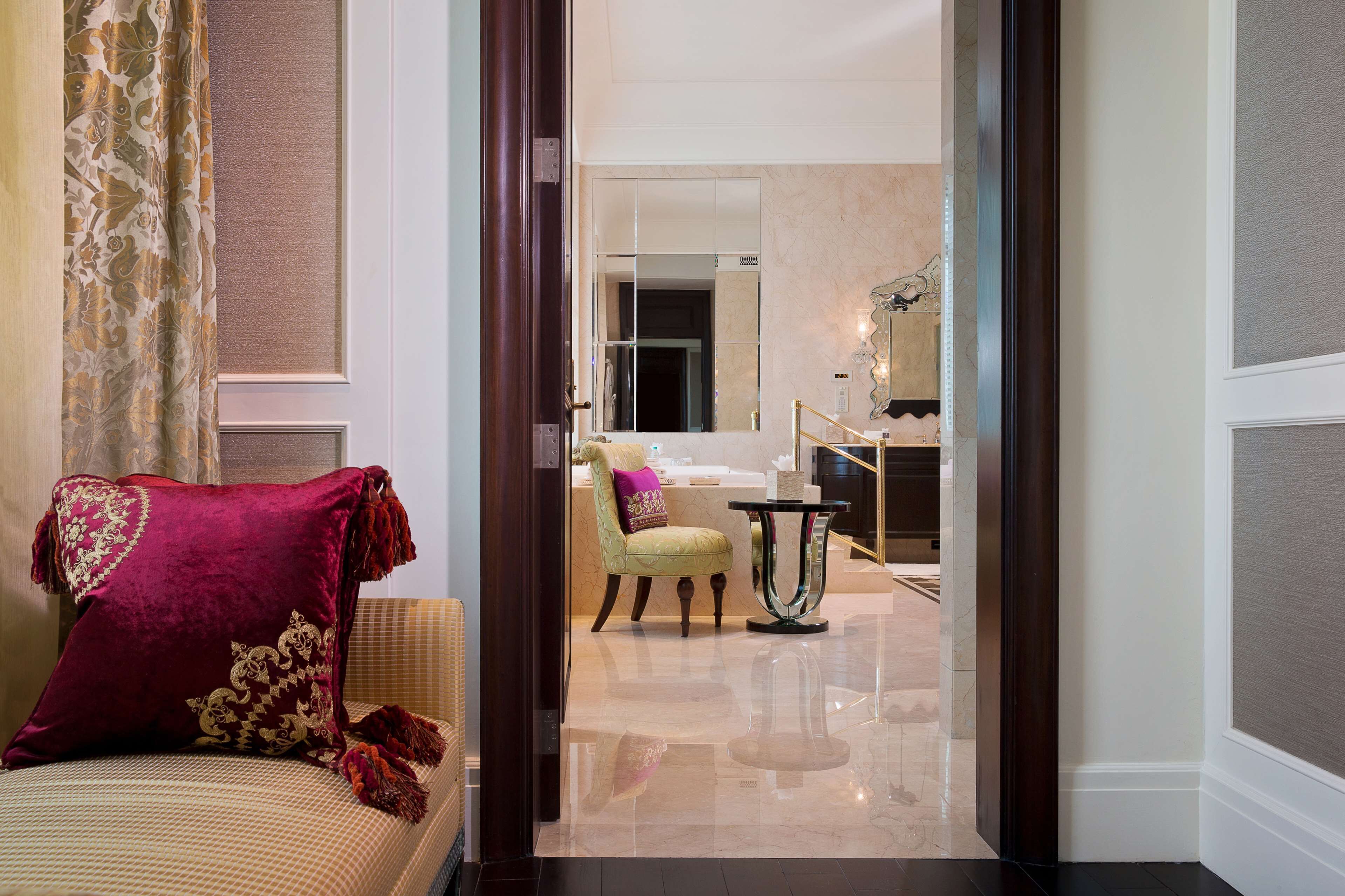 A hotel room with a plush red pillow, a green armchair, a small table, and a mirror.