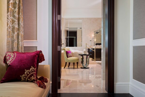 A hotel room with a plush red pillow, a green armchair, a small table, and a mirror.