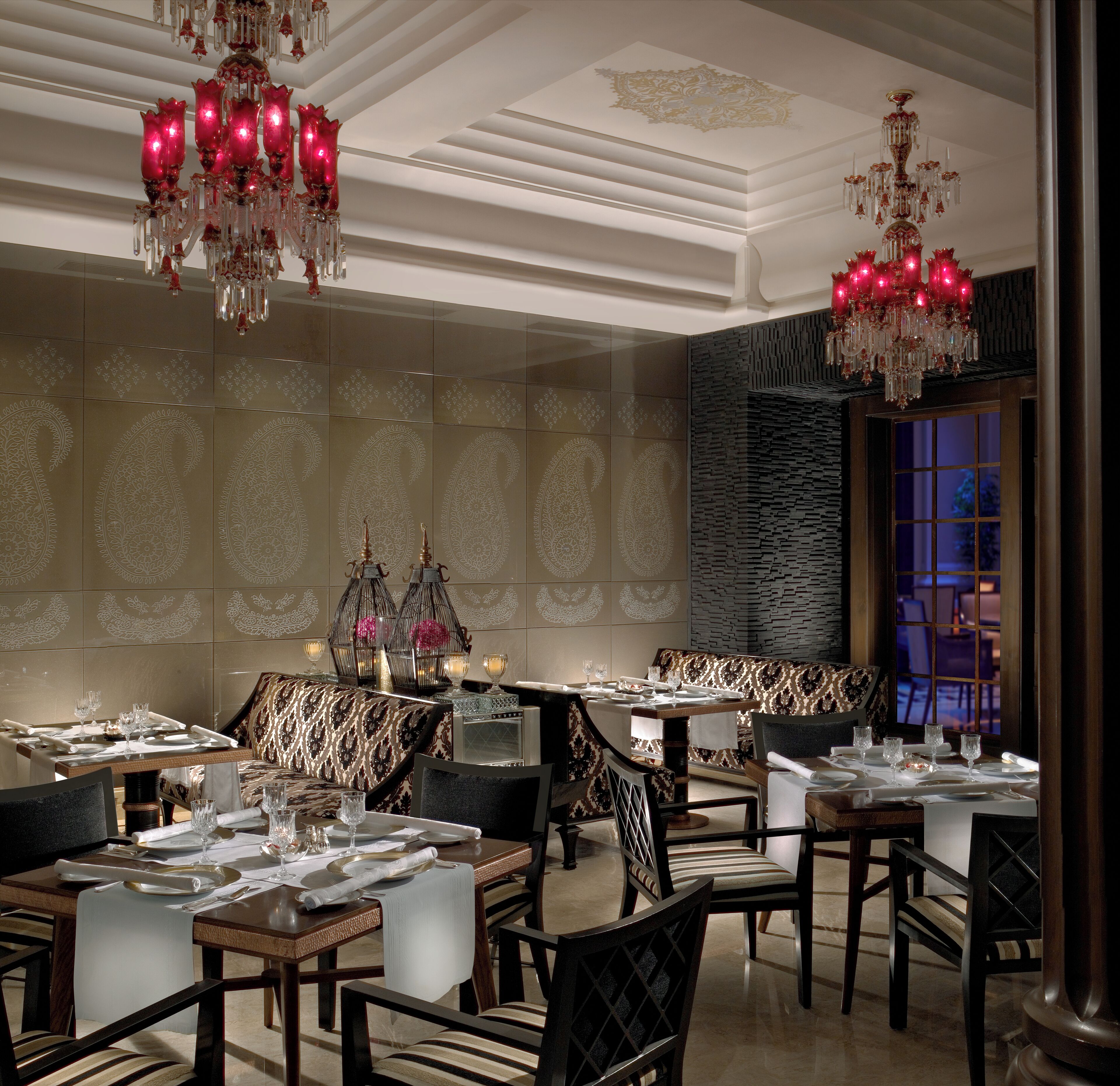 Un espace repas avec plusieurs tables dressées, de magnifiques lustres et des carreaux muraux décorés de motifs.