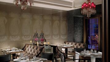 Un espace repas avec plusieurs tables dressées, de magnifiques lustres et des carreaux muraux décorés de motifs.