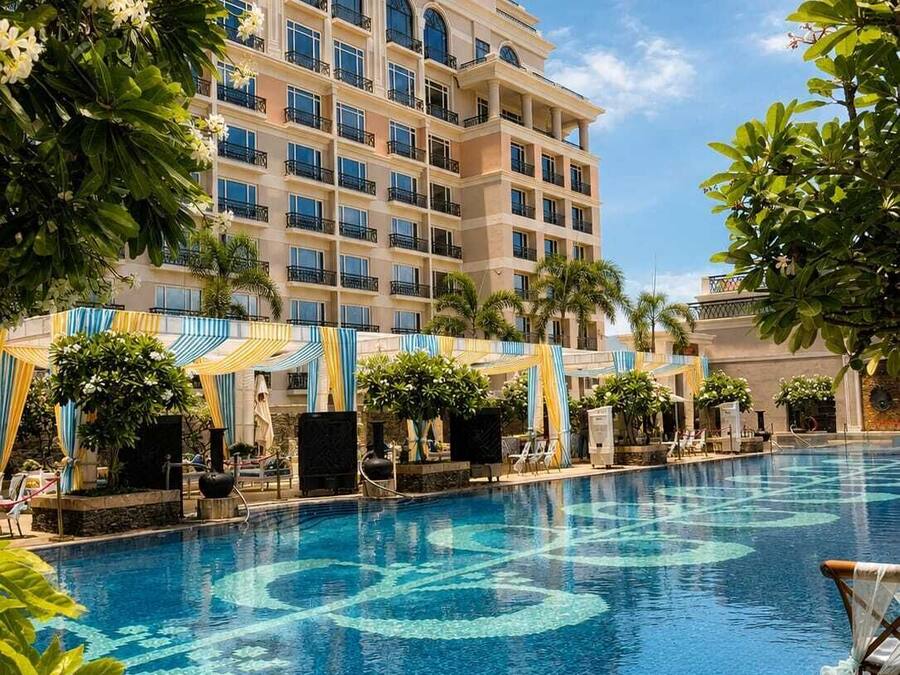 Een hotel met een zwembad, meerdere balkons en weelderige begroeiing.