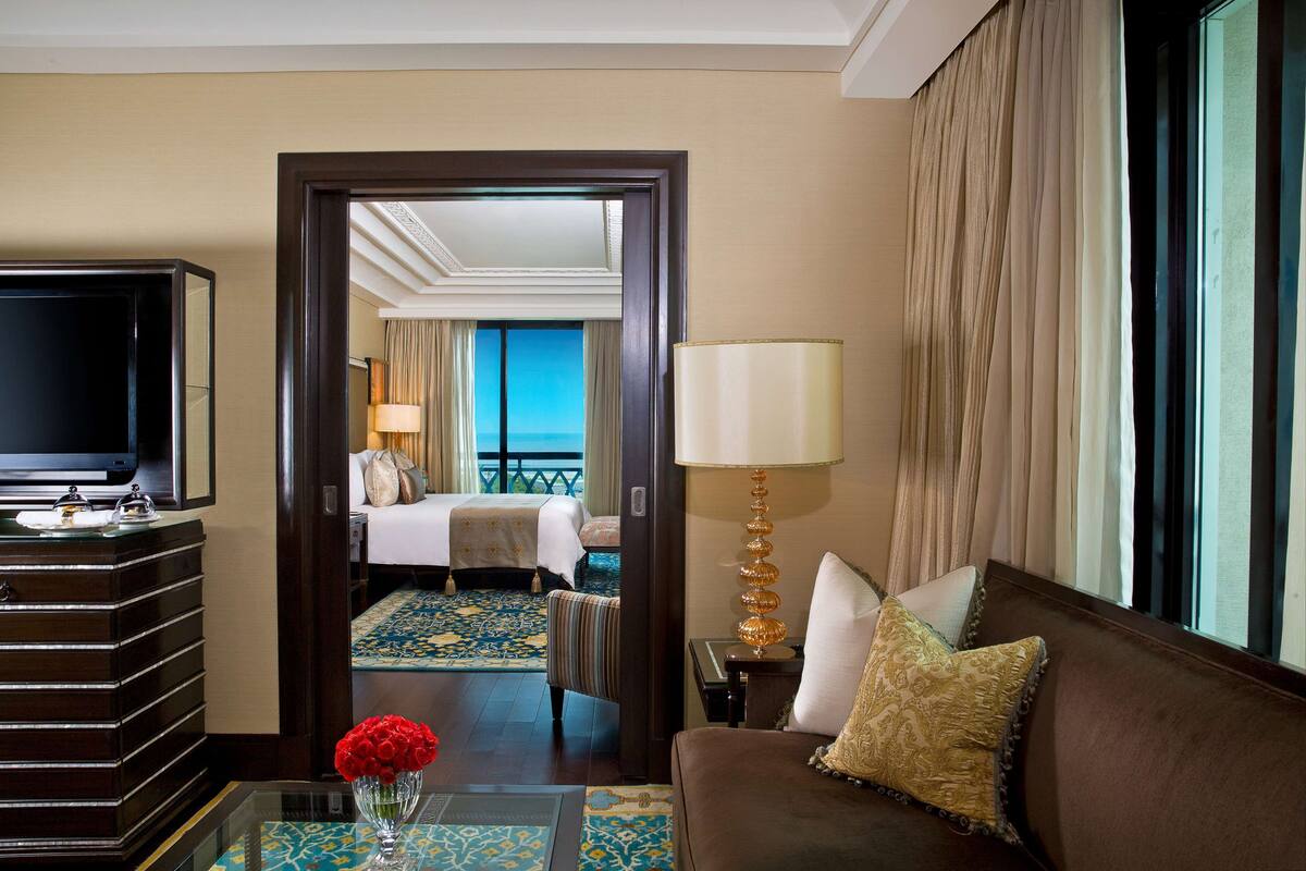 Ein Hotelzimmer mit Fernseher, einer Couch, einer Lampe, einer Vase mit Blumen und einem Bett mit Meerblick.