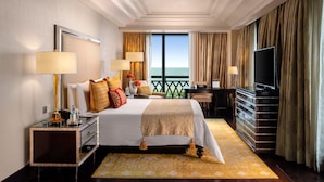 A hotel room with a large bed, two bedside tables, a desk with a chair, a TV, and a balcony with curtains. - The Leela Palace Chennai (Chennai)