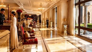 A hotel lobby with a marble floor, chandeliers, a reception desk, and a view of an outdoor courtyard.