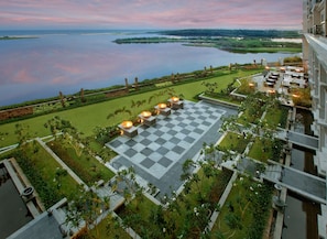 A rooftop terrace with a checkered floor, outdoor seating, and a view of a lake and distant land. - The Leela Palace Chennai (Chennai)