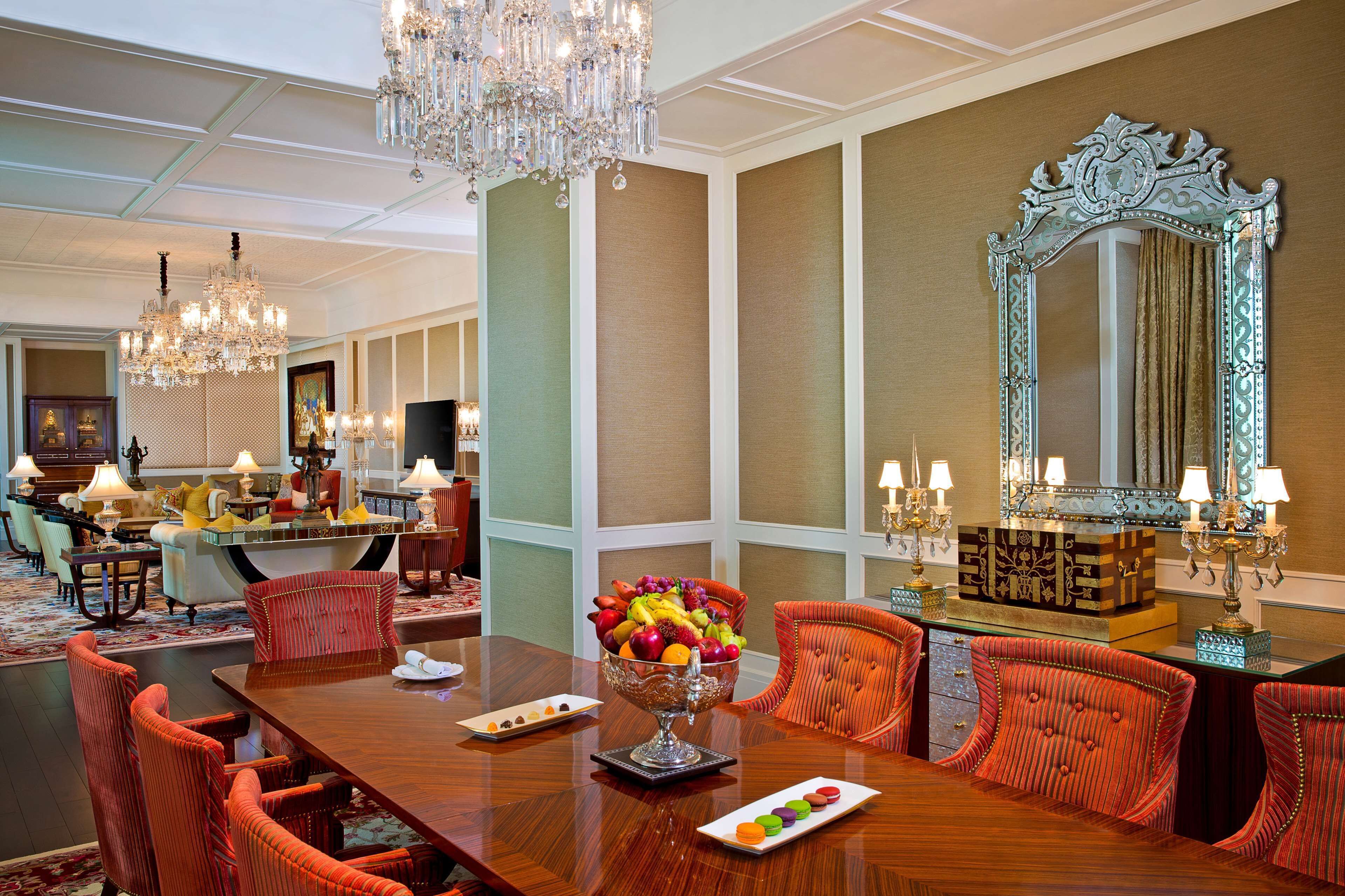 A dining area with a wooden table, orange upholstered chairs, a fruit bowl, and a large ornate mirror.