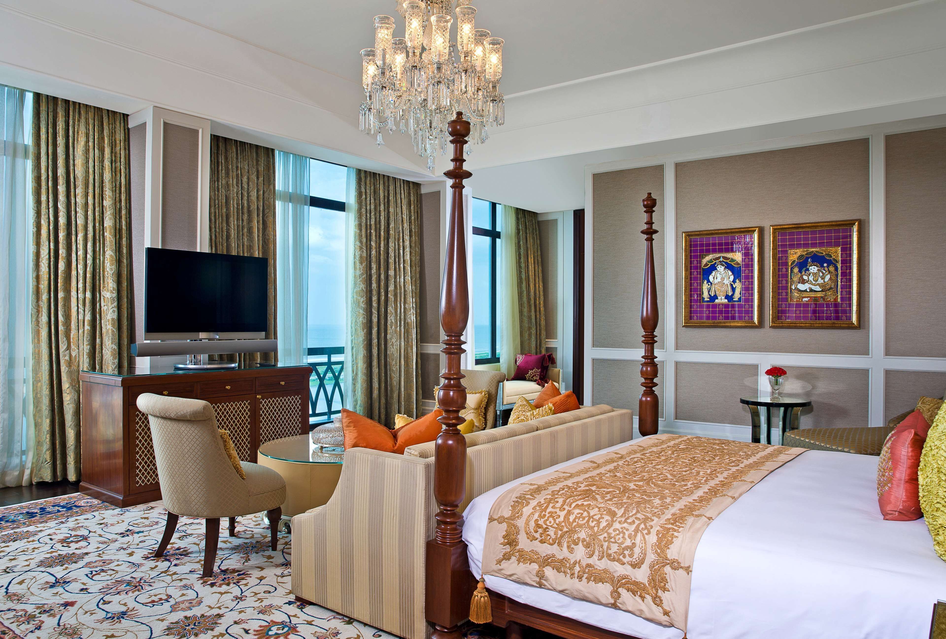 Quarto de hotel com uma cama grande, televisão, lustre e obras de arte nas paredes.