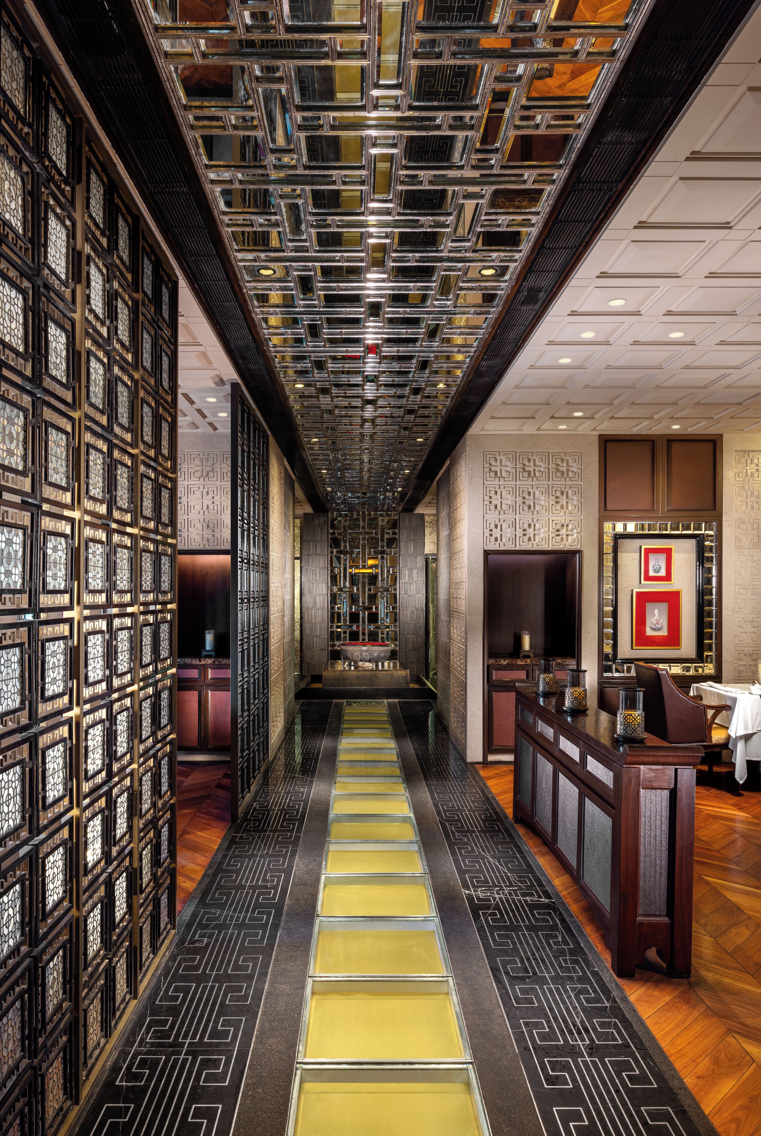 A hotel corridor with a patterned floor, a reception desk, and a wall with decorative panels.