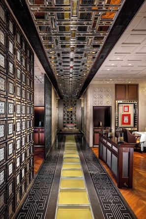 Corredor de hotel com piso estampado, balcão de recepção e painéis decorativos na parede.