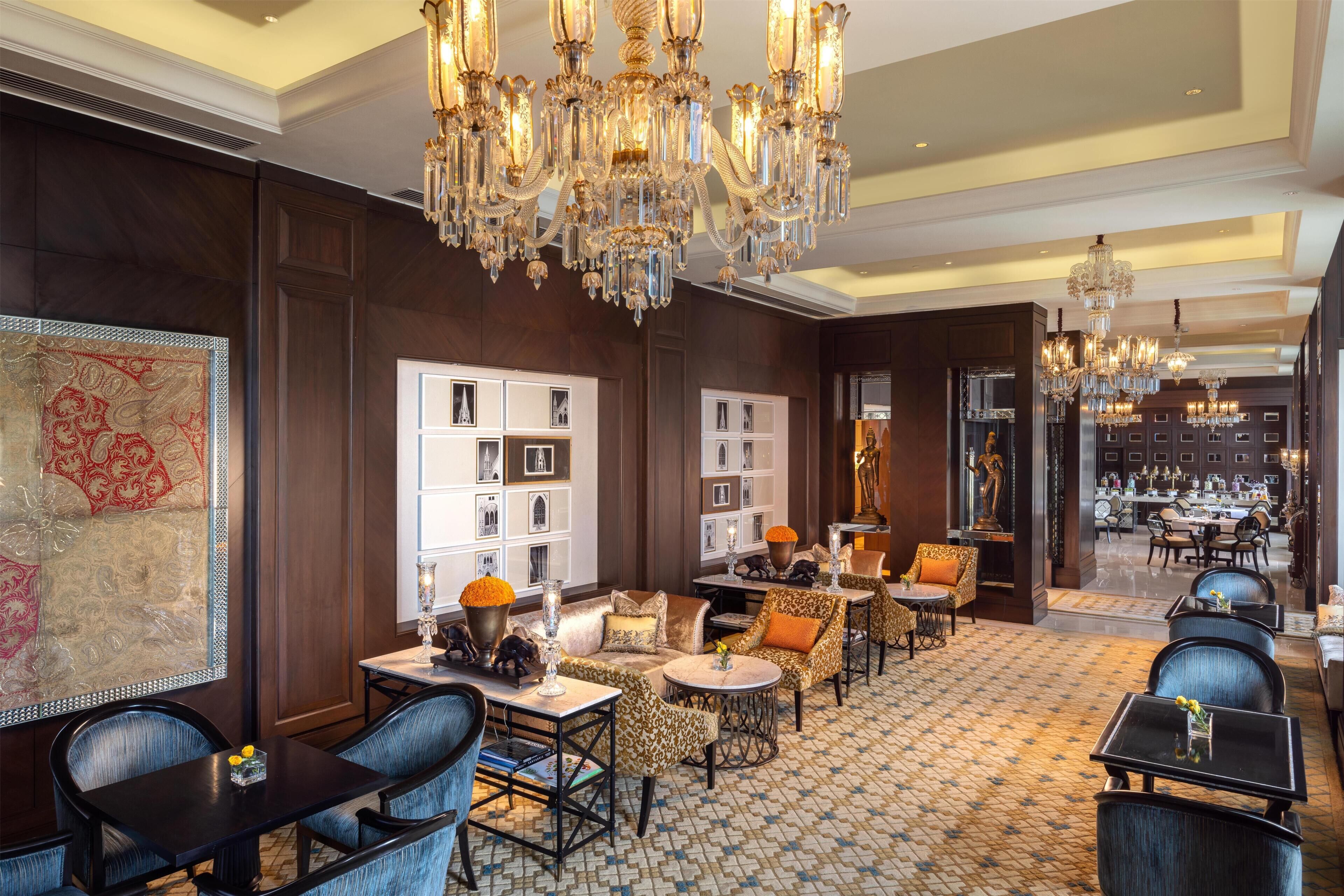 A luxurious hotel lobby with ornate chandeliers, plush seating, and a patterned floor.