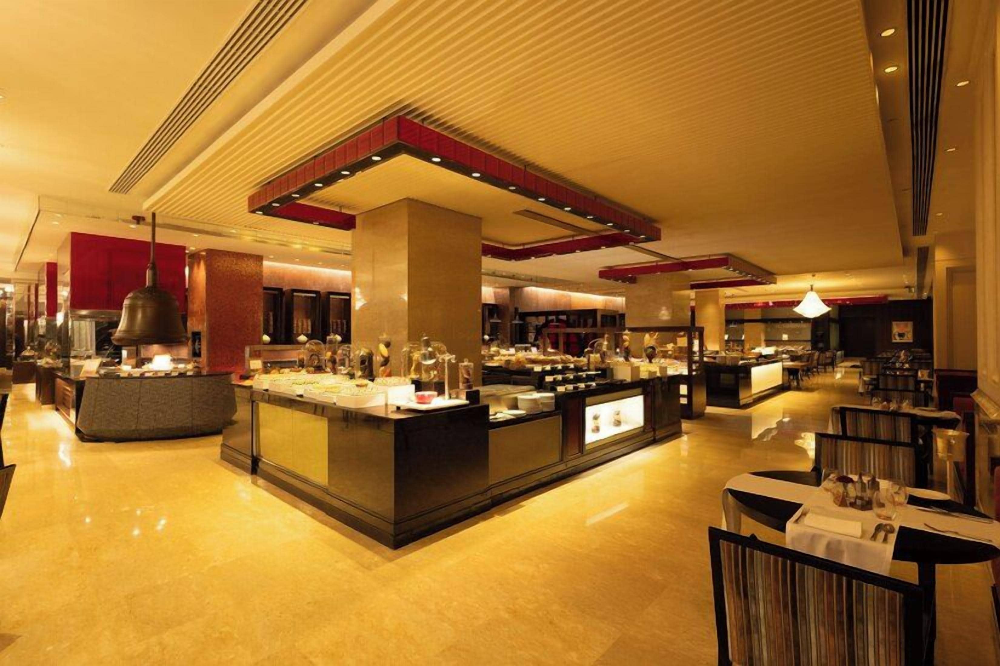 A spacious hotel lobby with a central bar area, seating arrangements, and a modern ceiling design.