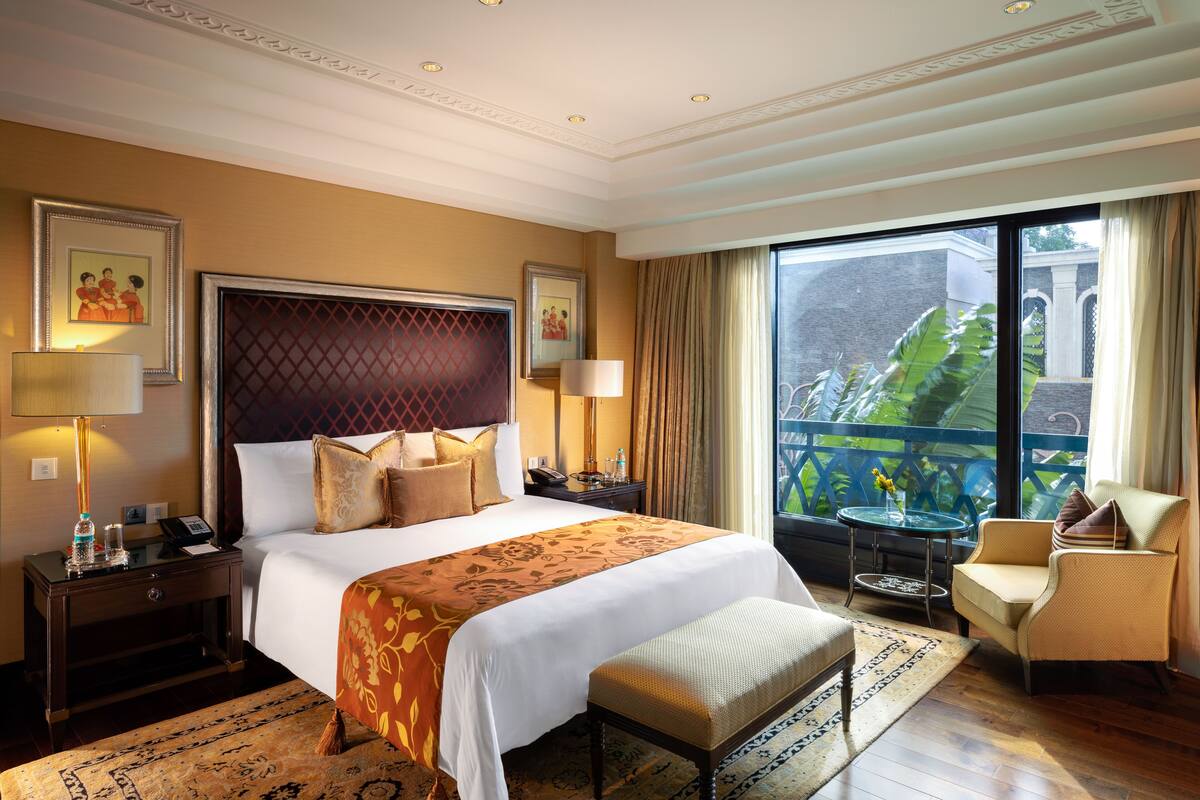 Ein Hotelzimmer mit einem großen Bett, einer Sitzecke mit Stuhl und Tisch, einem Balkon mit Aussicht und einer dekorativen Decke.