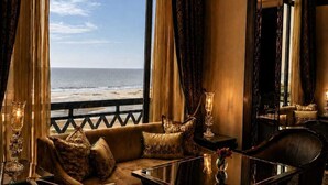 A room with a large window overlooking the sea, furnished with a sofa, chairs, and a table.