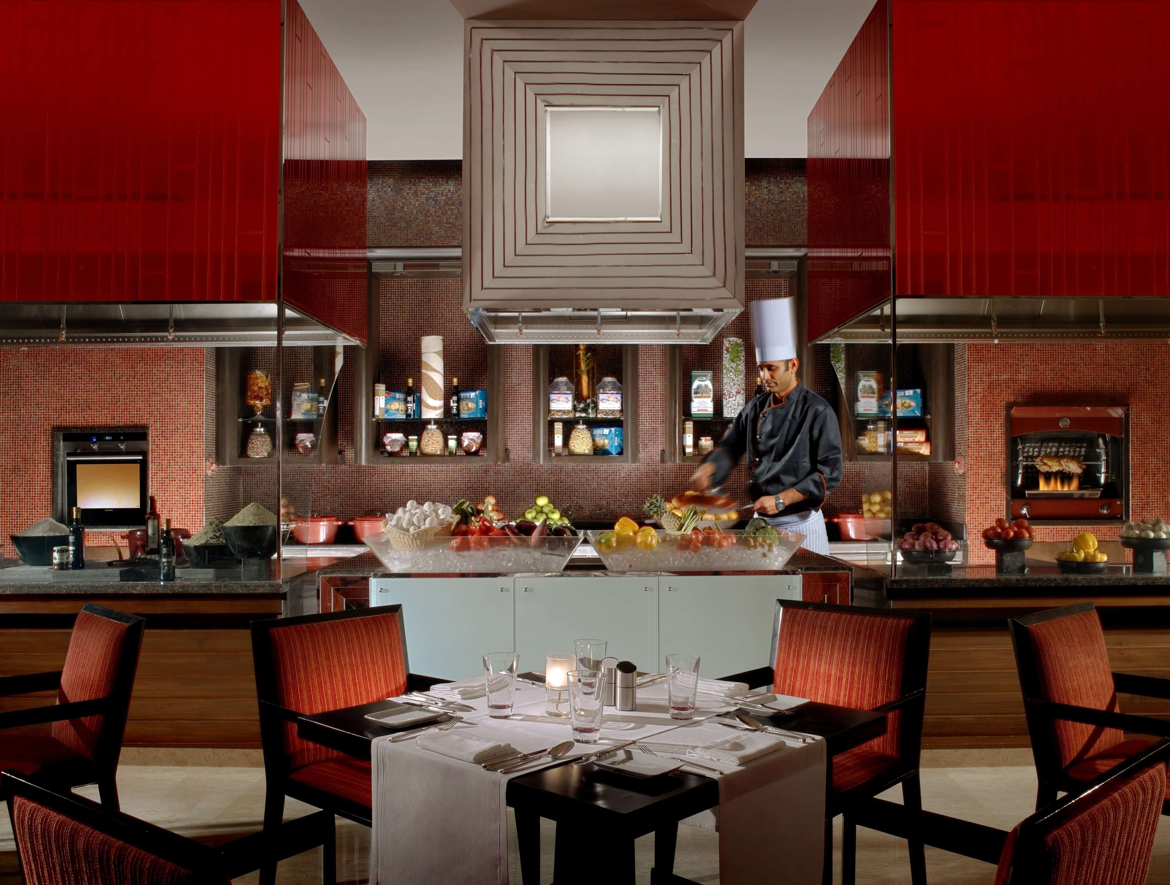 A restaurant with a chef preparing food, a bar area, and a dining table set for two.