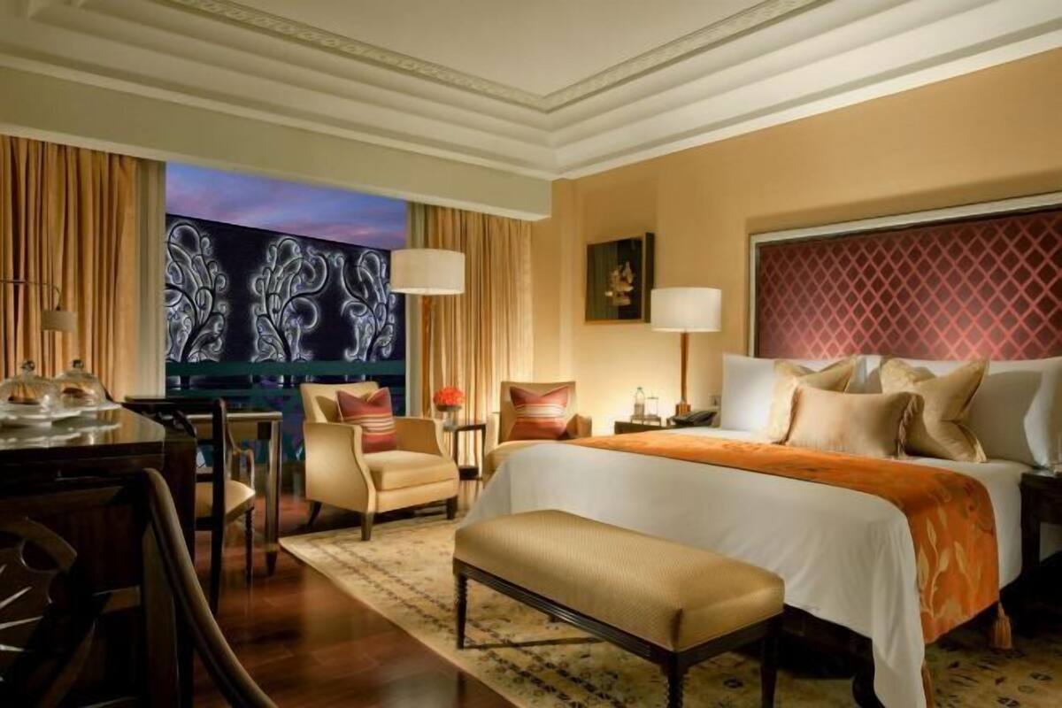 Ein Hotelzimmer mit Bett, Schreibtisch, Stuhl, Bank, Lampe und einem Gemälde an der Wand.