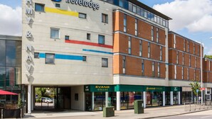 A Travelodge hotel with a modern design, featuring a prominent 'Travelodge' sign, a 'PIZZA' shop, and an 'EVANS CYCLES' store. - Travelodge Chelmsford (Chelmsford)