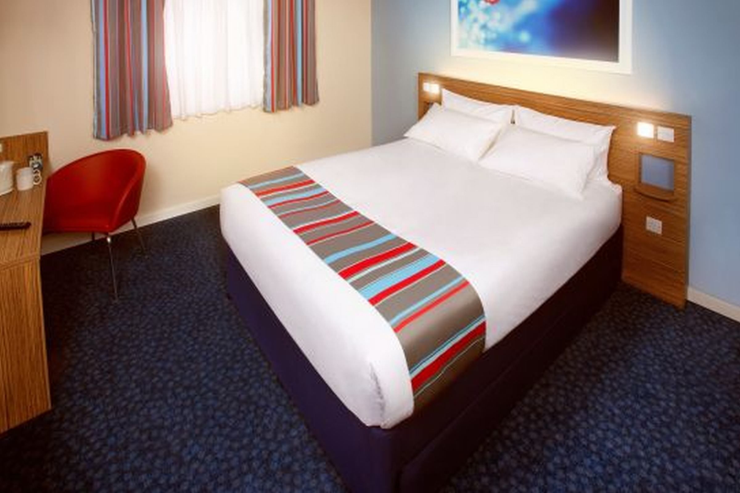 A hotel room with a bed, a desk, a chair, and a window with curtains.