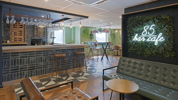 A bar area with a counter, stools, and a neon sign reading "85 bar cafe". - Travelodge Chelmsford (Chelmsford)
