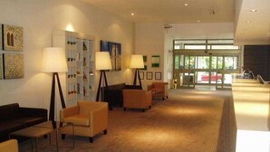Eine Hotelhalle mit Teppichboden, einem Empfangstresen und einer Sitzecke mit Sesseln und Lampen.