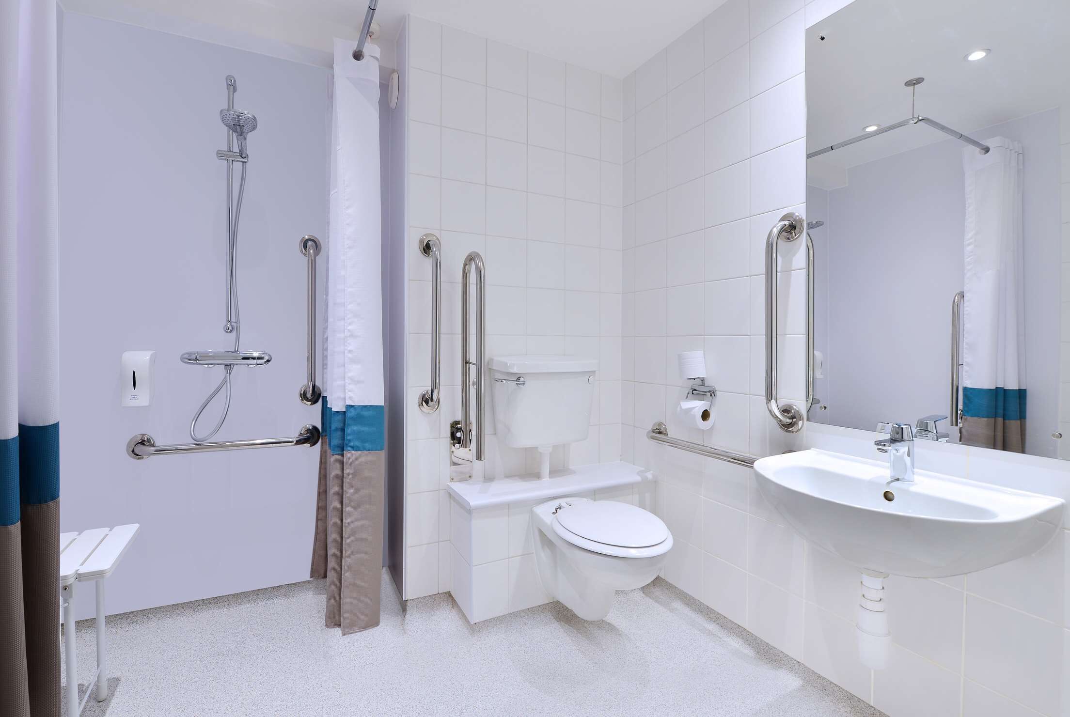 A modern bathroom with a shower, toilet, and sink, equipped with grab bars and a wheelchair-accessible bench.