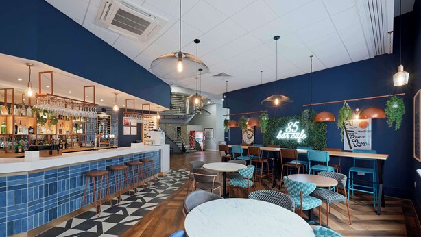 A modern cafe interior with a bar area, seating, and a staircase. - Travelodge Brighton Seafront (Brighton)
