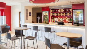 A bar area with stools, a counter, and shelves stocked with bottles. - Travelodge Maidstone Central (Maidstone)