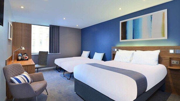 A hotel room with two beds, a desk, a chair, and a large abstract painting on the wall. - Travelodge Maidstone Central (Maidstone)