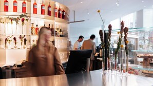 Un bar moderno con una barra curva, estantes con botellas y una vitrina de vidrio con flores.