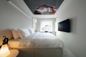 Una habitación de hotel moderna con una cama, un televisor de pantalla plana y un ventanal con vistas a la ciudad.