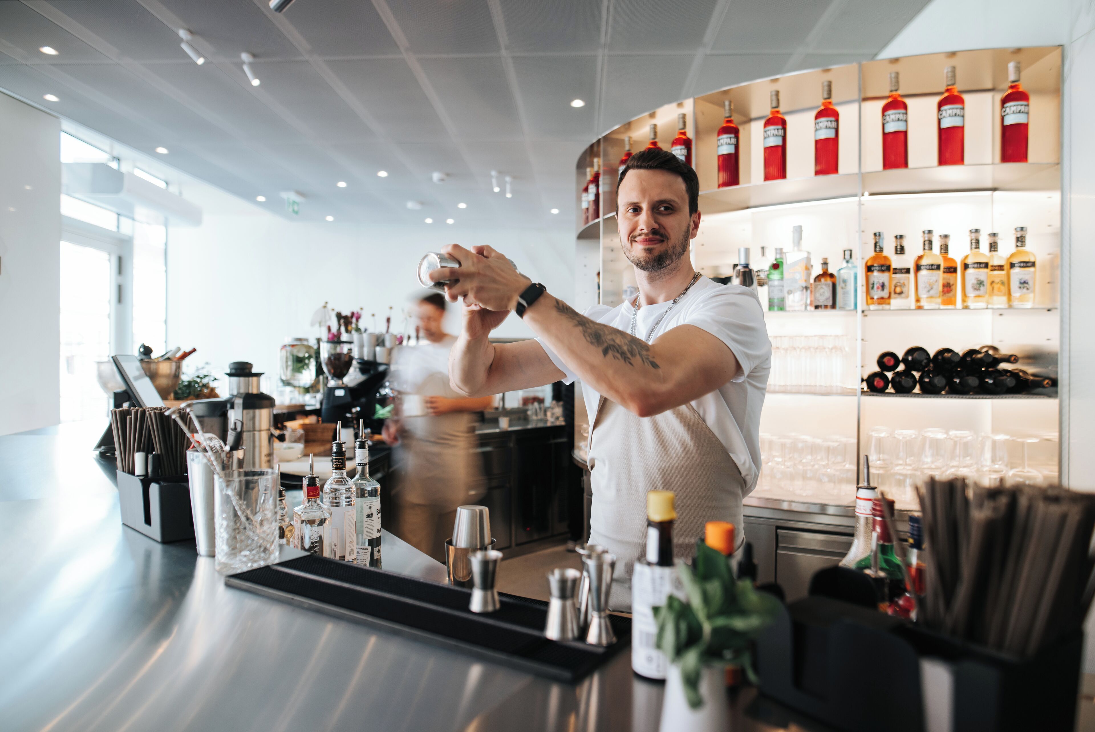 A bar area with a bartender preparing drinks, shelves with bottles, and a well-lit interior.