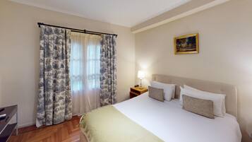 Habitación de hotel con cama, mesita de noche con lámpara, un cuadro en la pared y cortina con diseño de motivos naturales.