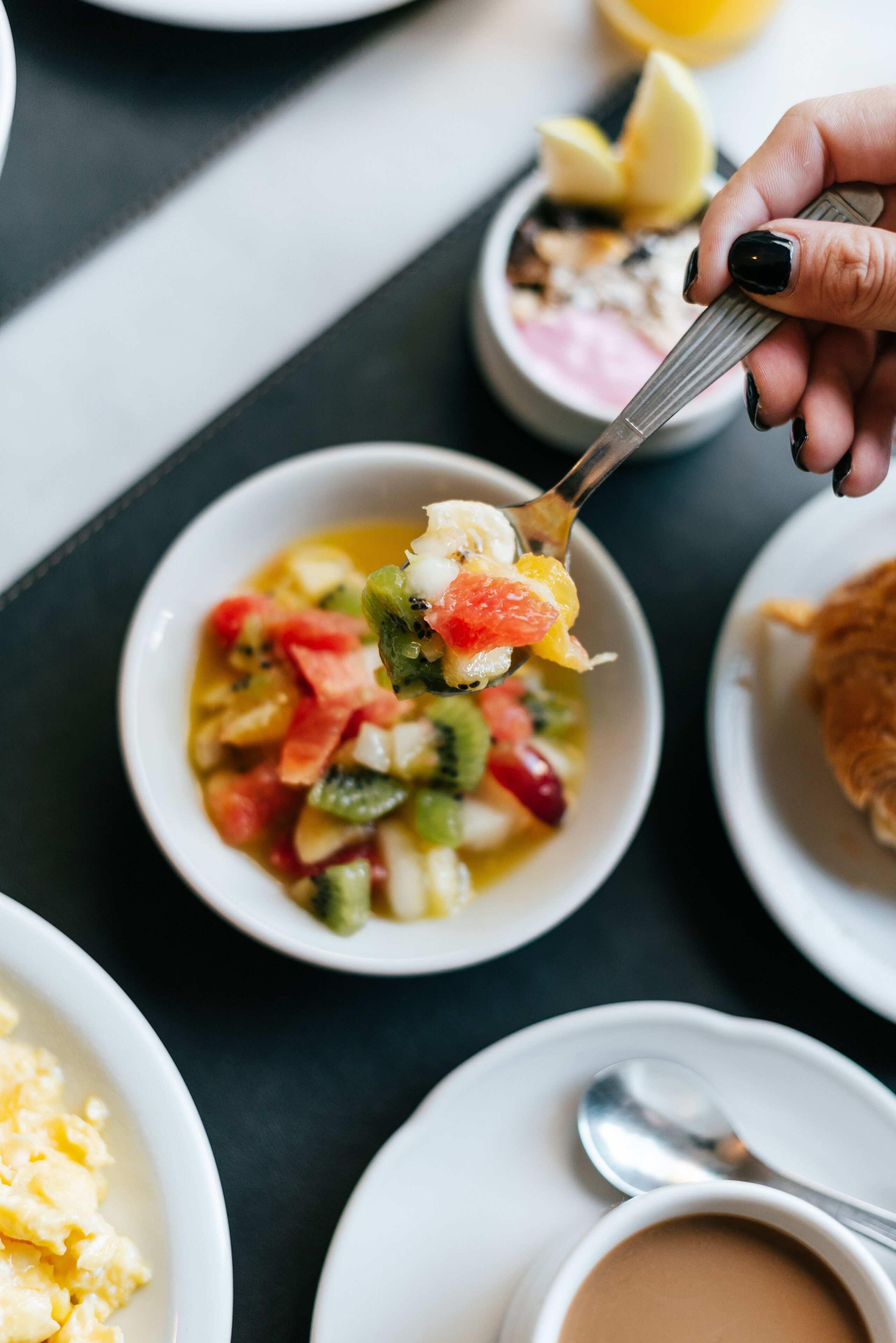 A close-up of a hand holding a spoon with a fruit salad.