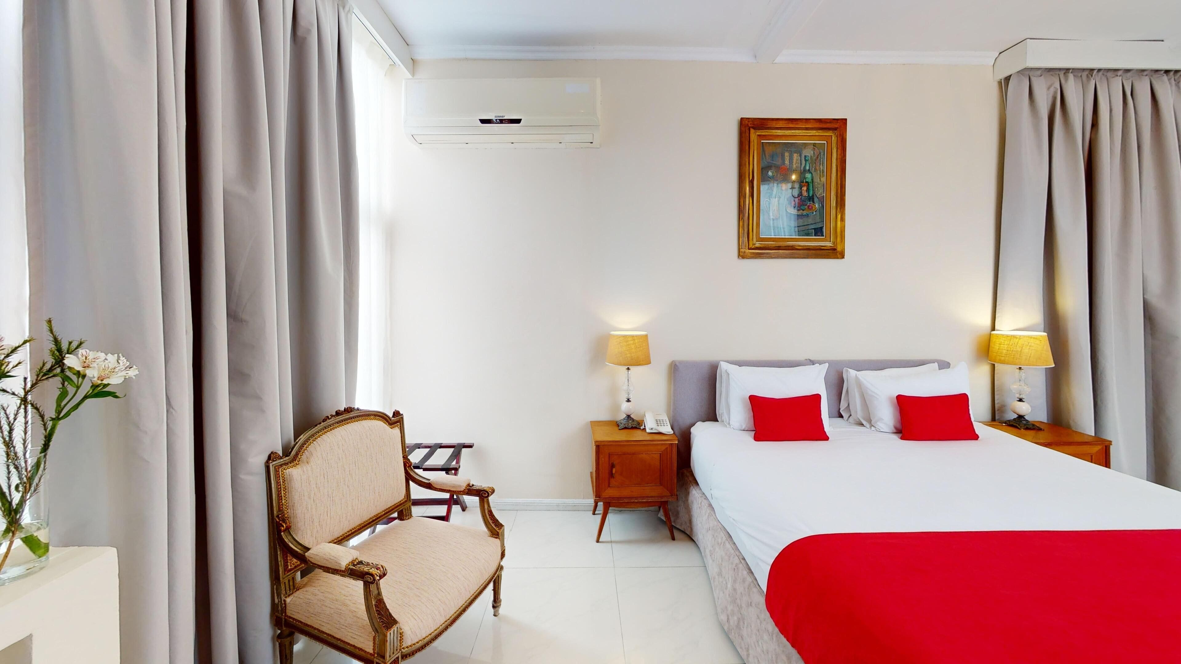 Habitación de hotel con cama, dos lámparas de noche, una mesita de noche, una silla y un cuadro en la pared.