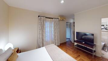 Habitación de hotel con cama, televisión, baño y un pasillo que conduce a otra habitación.