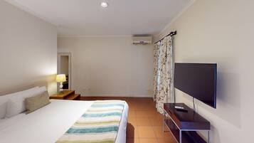 Una camera d'albergo con un letto, un comodino con una lampada, un televisore su un mobile e un condizionatore d'aria a parete.