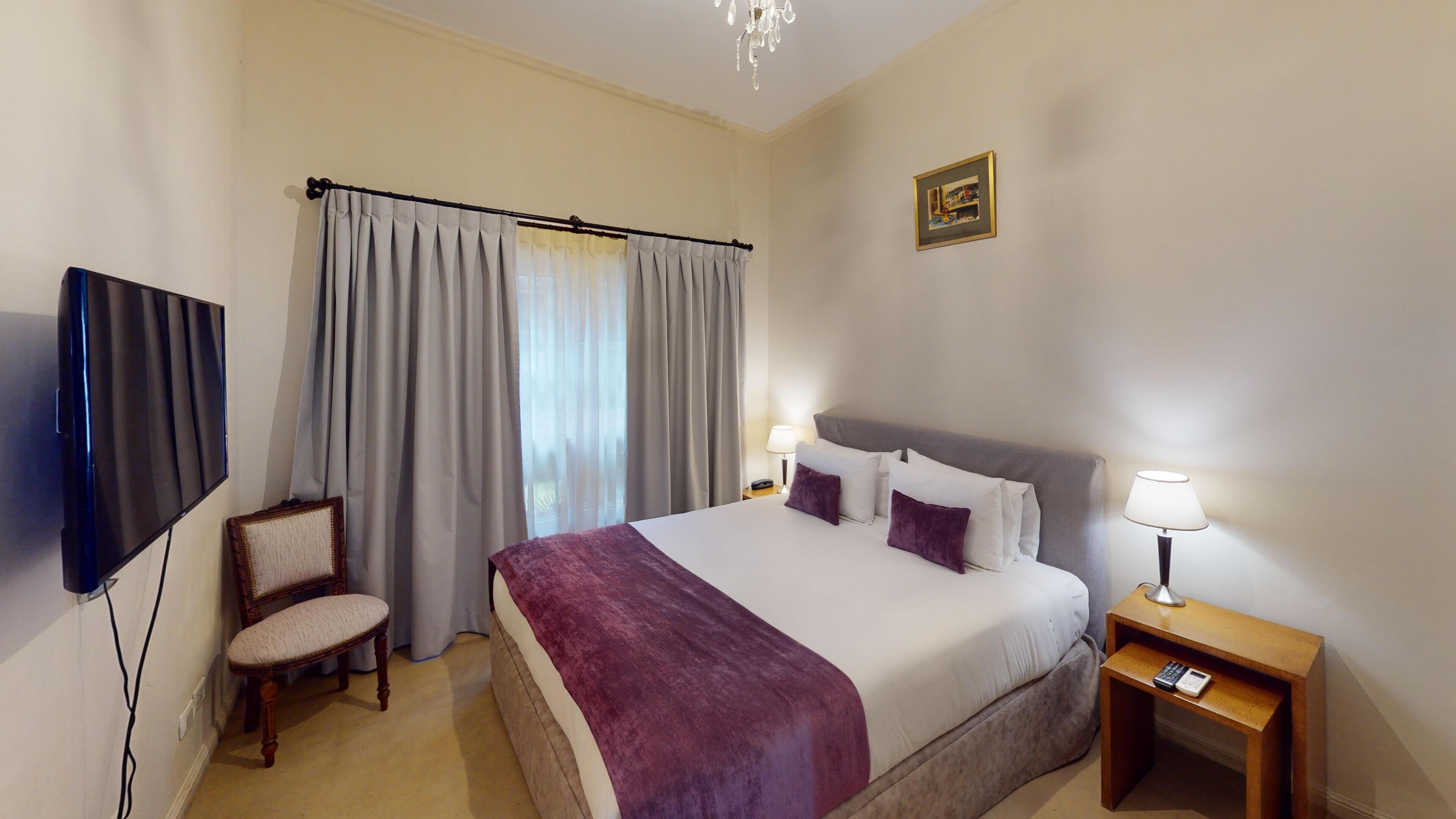 Habitación de hotel con cama, dos lámparas de noche, una silla, televisión e imagen en la pared.