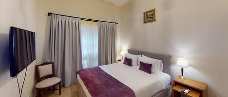 Habitación de hotel con cama, dos lámparas de noche, una silla, televisión e imagen en la pared.