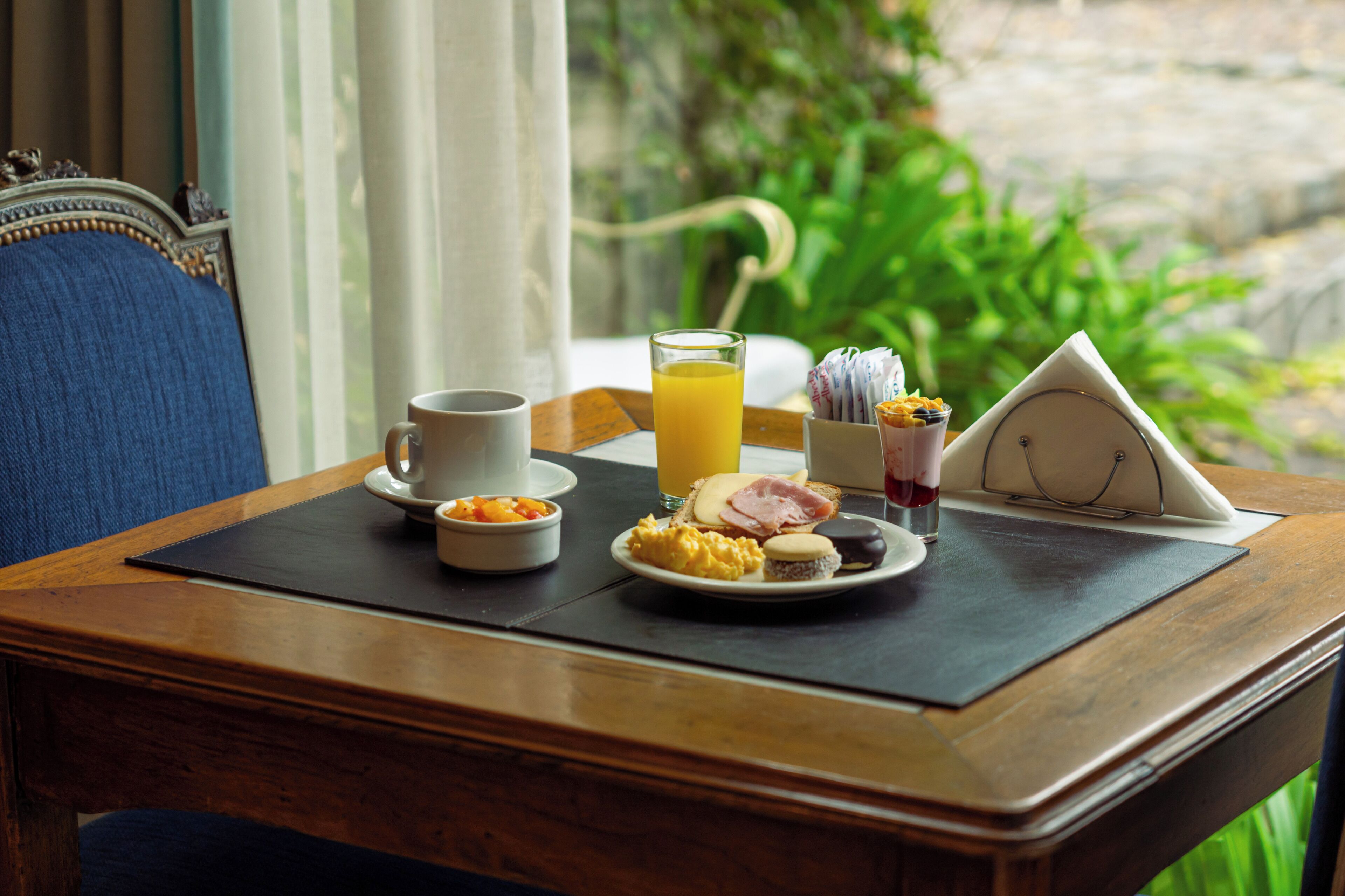 Una mesa de desayuno con una taza, jugo de naranja, huevos revueltos, jamón y un muffin.