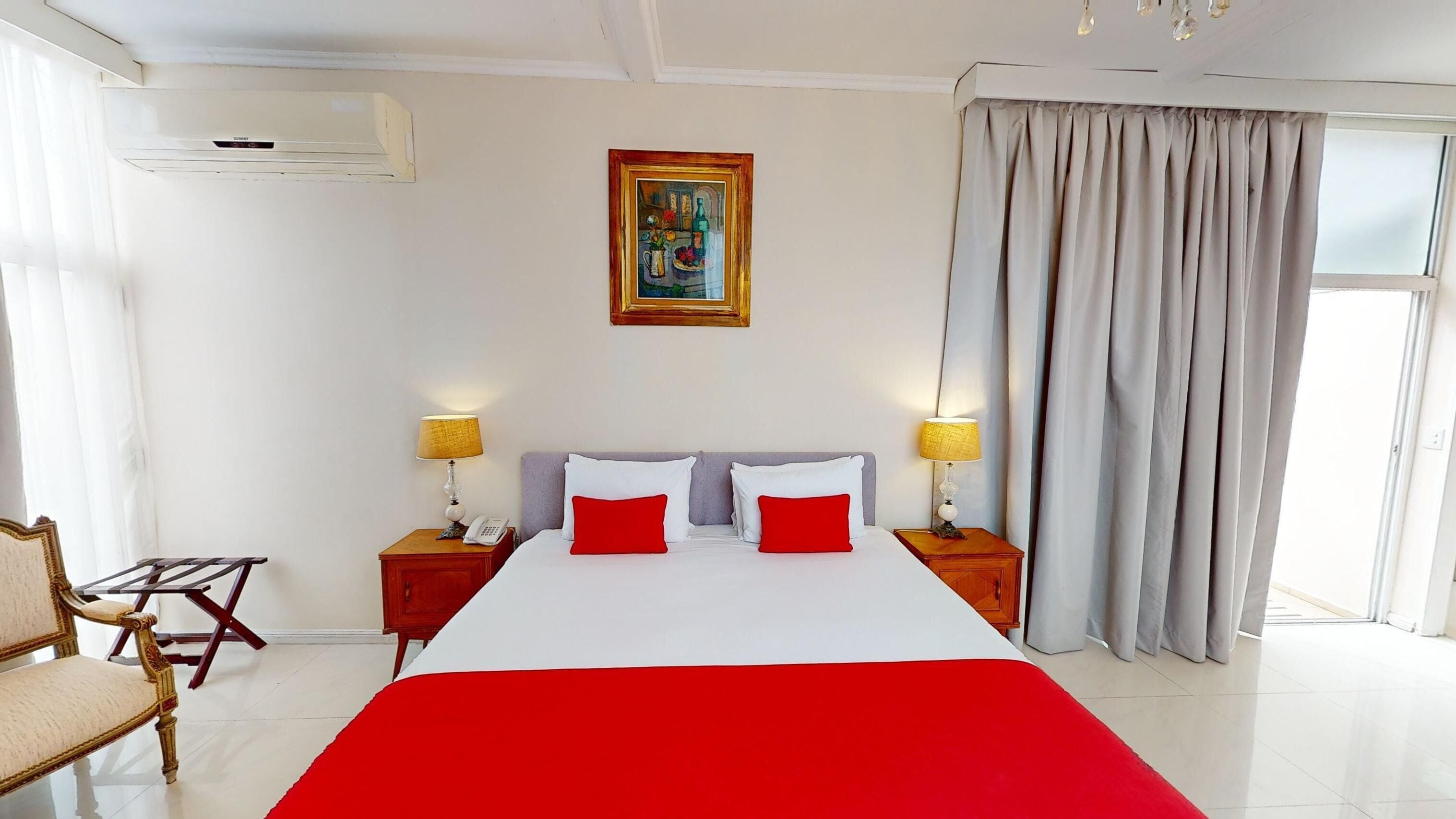 A hotel room with a large bed, two bedside tables with lamps, a chair, a painting on the wall, and a window with curtains.