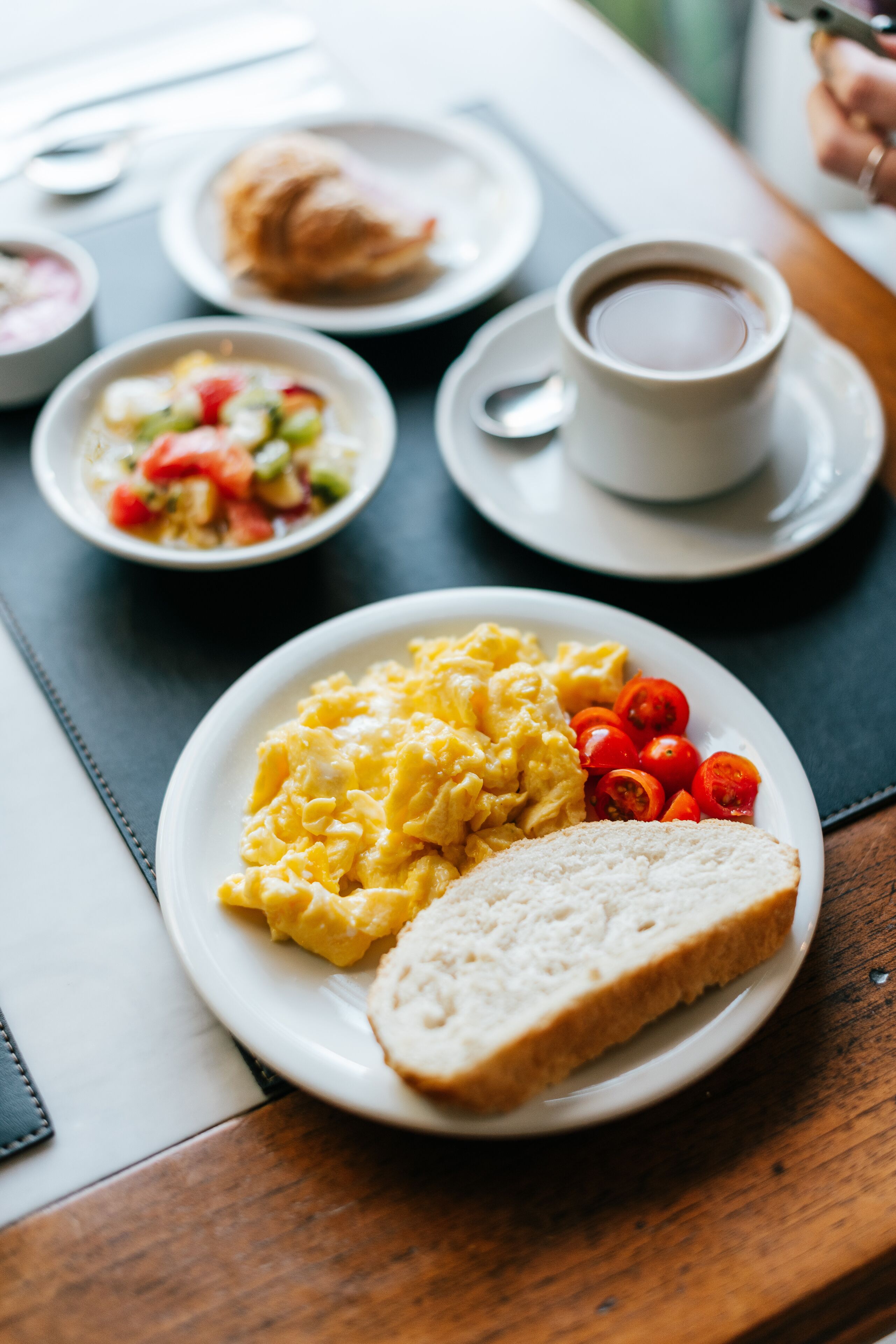 Una colazione con uova strapazzate, pomodorini, pane tostato e una tazza di caffè su un tavolo.