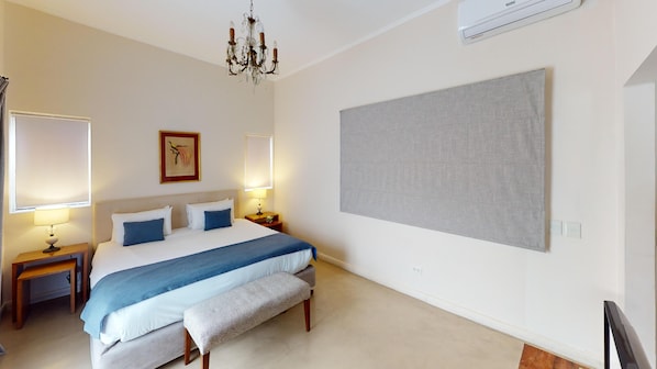 Un dormitorio con cama, mesitas de noche, un banco, una araña y una obra de arte grande en la pared.